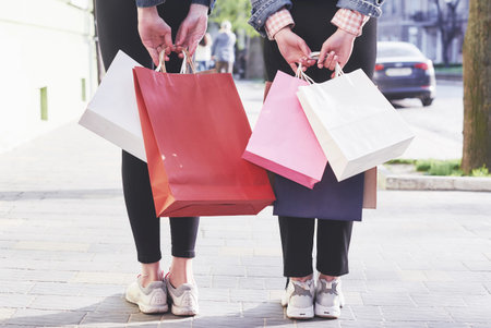Two young woman carrying shopping bags while walking in the street after visiting the stores.