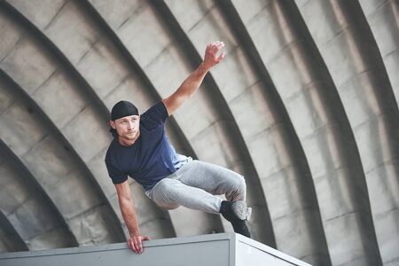 young man doing parkour jump in urban space in the city sunny spring summer dayの写真素材