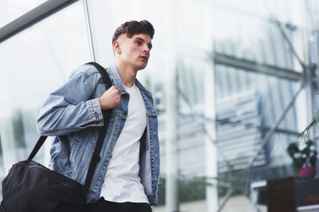 Young handsome man with a bag on his shoulder in a hurry to the airport.
