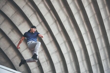 young man doing parkour jump in urban space in the city sunny spring summer dayの写真素材
