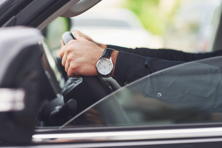 A businessman rides his car, moves on the wheel. Hand with watch
