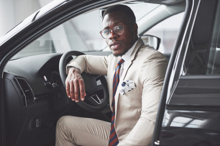 Stylish black businessman sitting behind the wheel of new luxury car. Rich african american man.