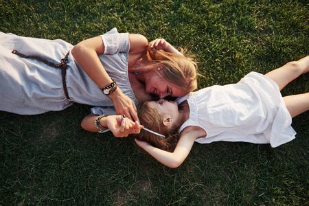 Happy little girl and her mother having fun outdoors on the green grass in sunny summer day.の写真素材