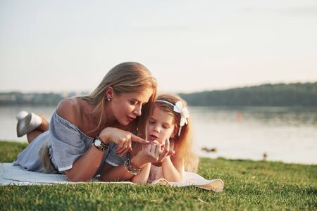 Attractive happy young mother lying with her cute daughter on the grass in the parkの写真素材