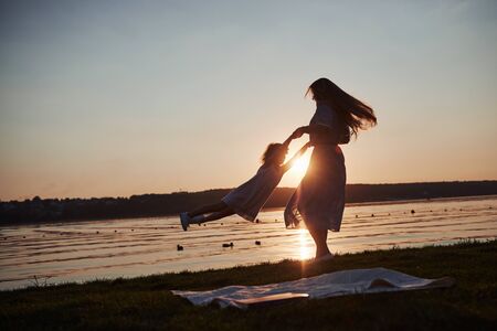 Mom plays with her baby on holidays near the ocean, silhouettes at sunset.の写真素材