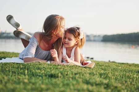Attractive happy young mother lying with her cute daughter on the grass in the parkの写真素材