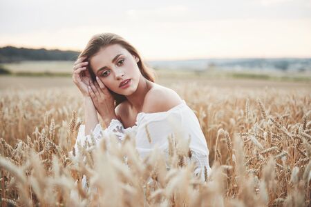 Beautiful girl in a field of wheat in a white dress, a perfect picture in the style lifestyleの写真素材