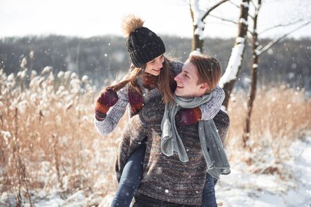 Couple has fun and laughs. kiss. Young hipster couple hugging each other in winter park. Winter love story, a beautiful stylish young couple. Winter fashion concept with boyfriend and girlfriend. It is snowingの写真素材