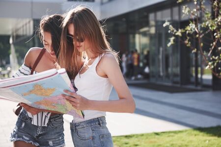 Two female tourist with map visiting a new city and is looking for a way to the hotel.の写真素材