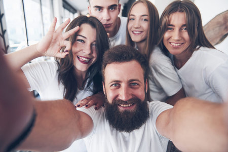 A group of people make a selfie photo in a cafe. The best friends gathered together at a dinner table eating pizza and singing various drinks.の写真素材
