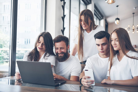 A group of young people with gadgets and a laptop arrange a brainstorm and communicate with each...
