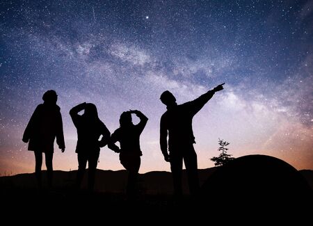 A silhouette of group people have fun at the top of the mountain near the tent during background of the Milky Way galaxy on a bright star sky tone.の写真素材