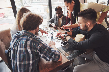 Group of creative friends sitting at wooden table. People having fun while playing board game.