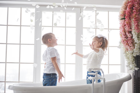 Child playing with rose petals in home bathroom. Little girl and boy fawing fun and joy together....