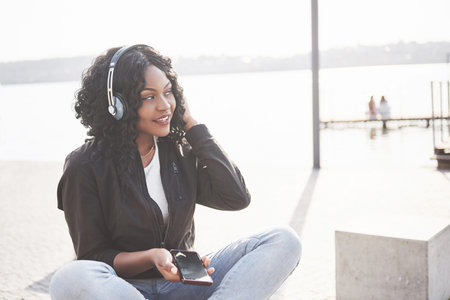 Portrait of a beautiful young pretty African American girl sitting on the beach or lake and...