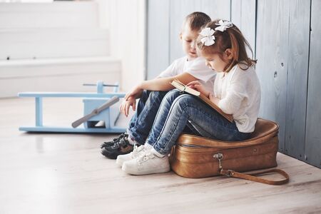 Ready to big travel. Happy little girl and boy reading interesting book carrying a big briefcase. Freedom and imagination concept.の写真素材