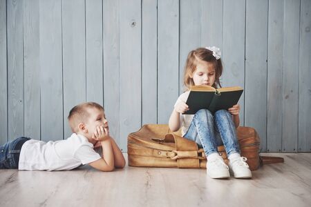 Ready to big travel. Happy little girl and boy reading interesting book carrying a big briefcase. Freedom and imagination concept.の写真素材