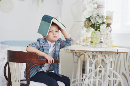 Photo of diligent schoolboy with book on his head doing homework.の写真素材