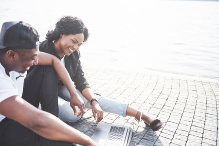 Two happy friends of students or business partners are sitting outdoors and enjoying a laptop.の写真素材