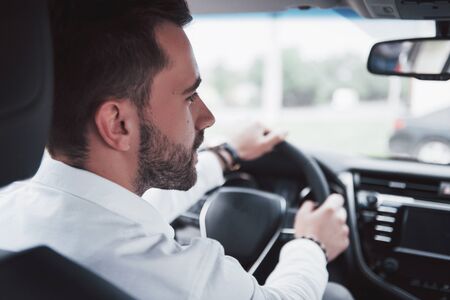 Rear view of confident young businessman sitting at the wheel of his new car.の写真素材