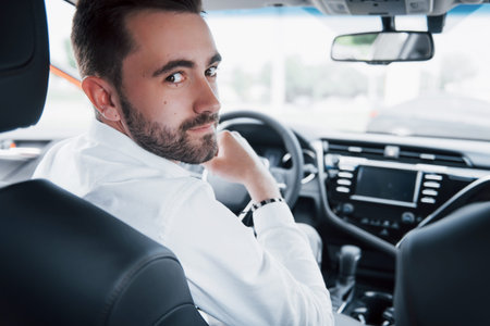 Rear view of confident young businessman sitting at the wheel of his new car.