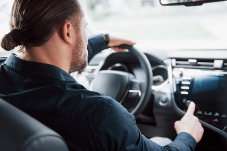Rear view of confident young businessman sitting at the wheel of his new car.