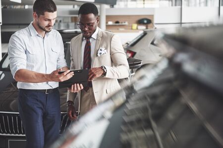 A young black businesswoman signs documents and buys a new car. The car dealer is standing next to him.の写真素材