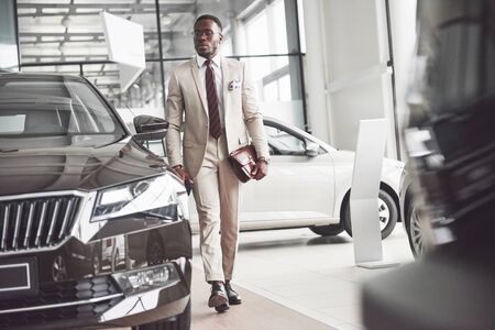 Young black businessman on auto salon background. Car sale and rent concept. Rich african american man.の写真素材