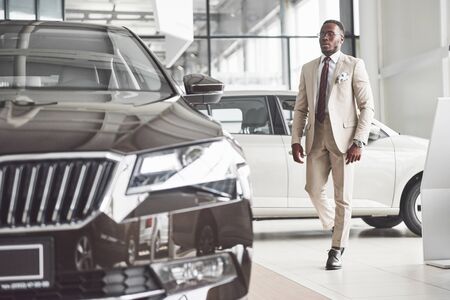 Young black businessman on auto salon background. Car sale and rent concept. Rich african american man.の写真素材