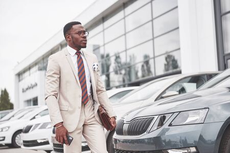 Visiting car dealership. Casual black business man in a suit near the car.の写真素材