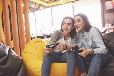 Twin sister sisters play on the console. Girls hold joysticks in their hands and have fun.