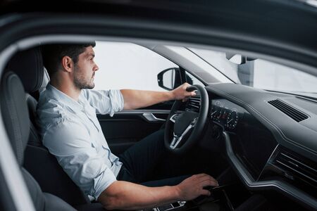 A young man sits in a newly bought car holding his hands on a rudderの写真素材