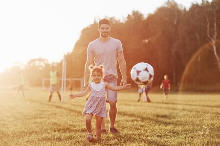 Watch cameramen, hes not soccer player. Photo of dad with his daughter at beautiful grass and woods at background.の写真素材