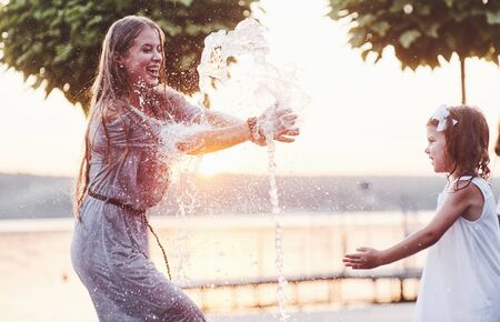 Catch the water. In a hot sunny day mother and her daughter decide to use fountain for cooling themselves and have fun with it.の写真素材