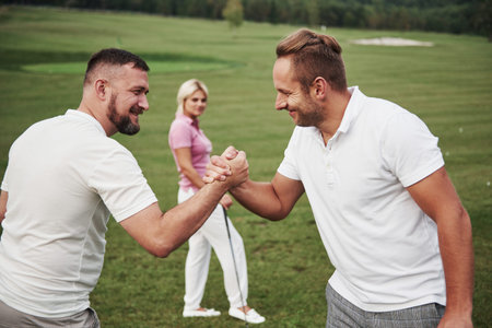 Three players play on the golf course. The team congratulates and shakes hands with each other.
