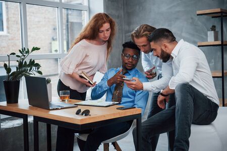 Using smartphone for finding information. Group of multiracial office workers in formal clothes talking about tasks and plans.の写真素材