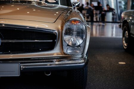 Close-up of the left headlight of retro beige cabriolet car with chrome side mirror, bumper and radiator trim.の写真素材