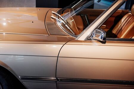 Side, lose up view of beige retro cabriolet car steering wheel with chrome window trim and windshield washer, mirror, shiny hood, left door and leather interior.の写真素材