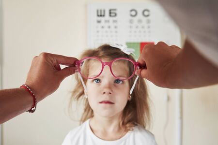 Kid looking at pink glasses with board for checking vision at background.の写真素材