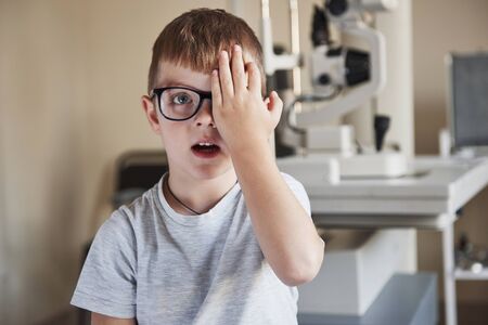 Tells what he see. Little boy covering his eye and having a look at the eye in the clinic.の写真素材