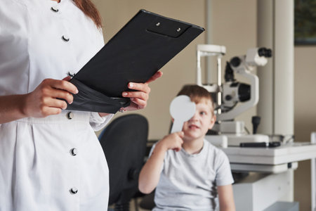 Standing and writing. Doing testing in the oculist office with child. Doctor notes data.