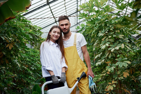 Young couple of workers posing for the photo in the greenhouse with water canister.の写真素材
