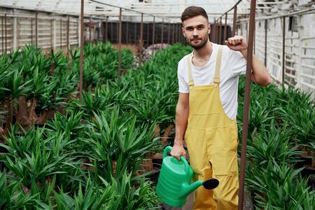 Photo of bearded young man in the greenhouse and holding water canister.の写真素材