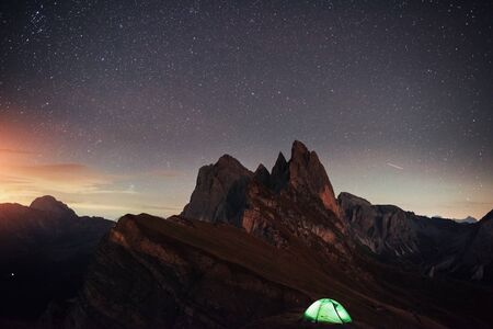 Sunset in yellow clouds. Night photo of Seceda dolomites mountains. Tourists resting in the green tent.の写真素材