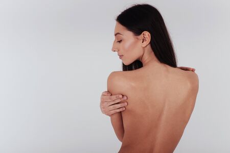 Detailed studio shoot. Young woman with perfect body and smooth skin stands with her back on the white background.の写真素材