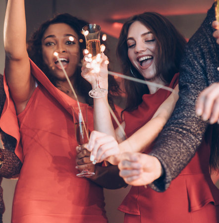 Hands up and partying. Multiracial friends celebrate new year and holding bengal lights and glasses...