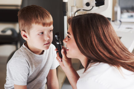 Woman in process of checking the young kids eyes and smiles during the process.