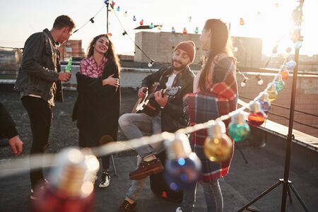 Playing music and singing. Rooftop party with alcohol and acoustic guitar at sunny autumn day.の写真素材