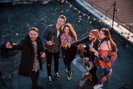 Happy together. Top view of a young friends that take selfie while have fun at the roof with decorative colorful light bulbs.の写真素材