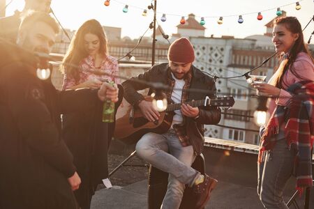 Front view. Guitar guy with friends on the roof at sunny day.の写真素材